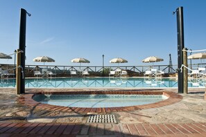 A swimming pool with a brick border, surrounded by white lounge chairs and umbrellas.