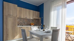 Een eetgedeelte met een witte tafel en stoelen, een keuken met blauwe muren en houten kasten, en een balkon met uitzicht.