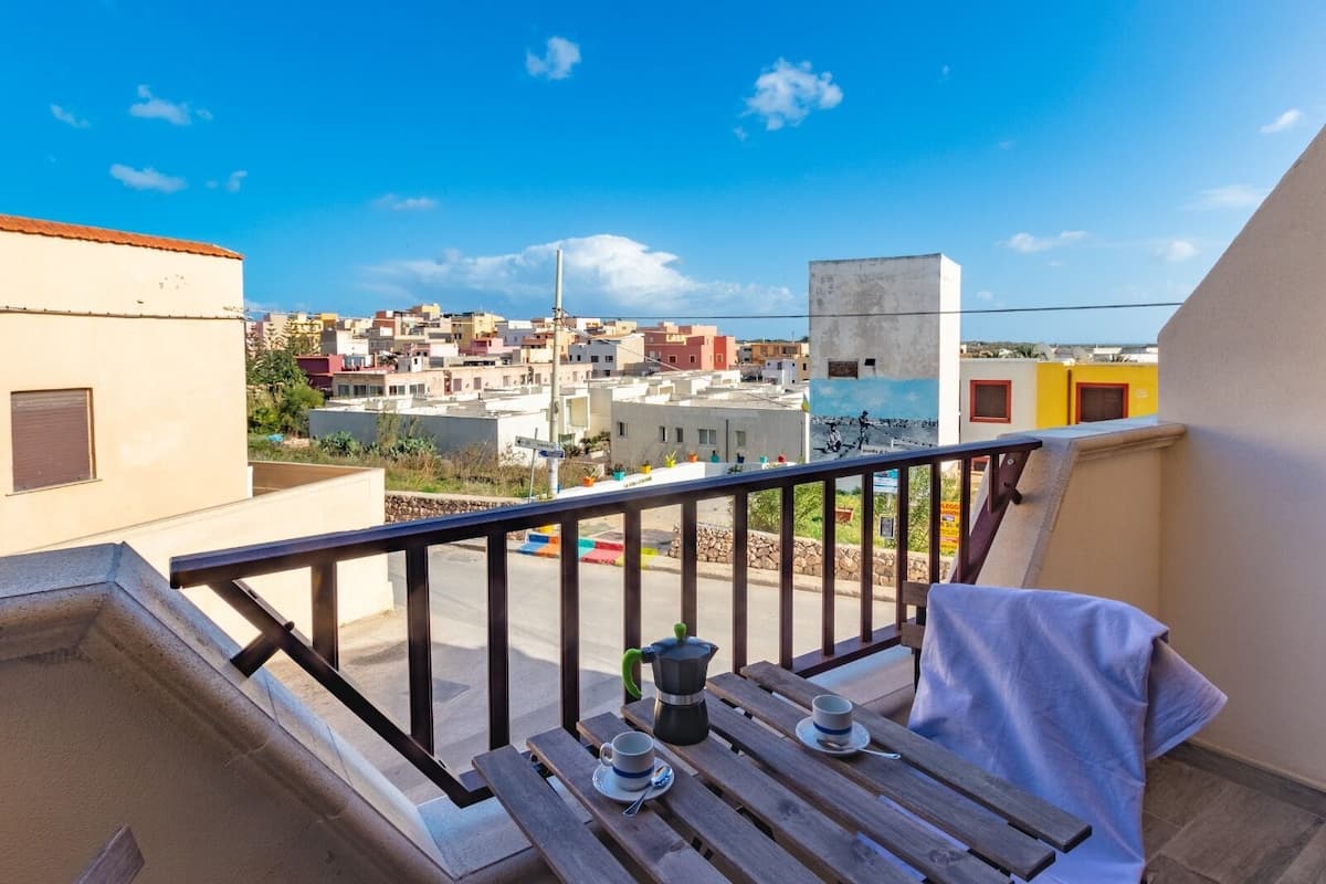 A balcony with a view of a town, a table with a cup and saucer, and a potted plant.