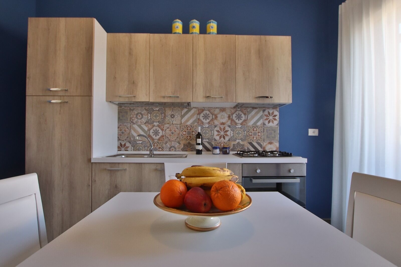 A kitchen with wooden cabinets, a tiled backsplash, and a fruit bowl on the table.