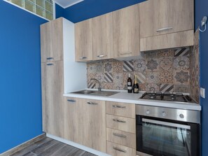 Cocina moderna con armarios de madera, encimera blanca, estufa a gas y salpicadero de azulejos.