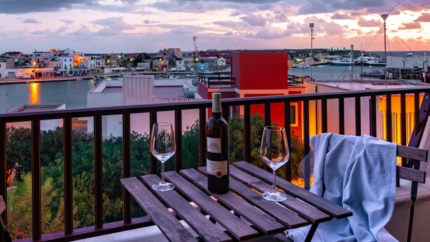 Een balkon met een houten tafel, twee wijnglazen en een fles wijn.