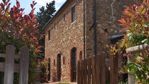 A stone building with a wooden gate, a brick pathway, and a grassy area. - Panoramic three-room apartment with garden, swimming pool, tennis, in the countryside near the sea and services  (campiglia marittima)
