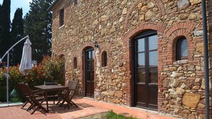 A stone building with a patio area featuring a wooden table and chairs. - Panoramic three-room apartment with garden, swimming pool, tennis, in the countryside near the sea and services  (campiglia marittima)