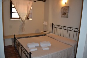A bedroom with a bed, a window with a curtain, a bedside table with a lamp, and a wall-mounted picture.