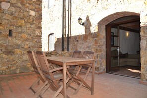 An outdoor patio with a stone wall, wooden table and chairs, and a glass door leading inside.