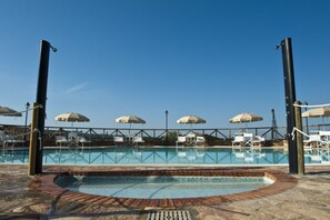 A swimming pool with a brick border, surrounded by lounge chairs and umbrellas.