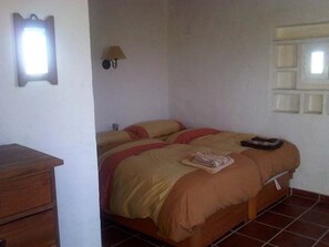 Une chambre à coucher avec un lit, une commode en bois, une lampe fixée au mur et une fenêtre donnant sur un beau paysage.