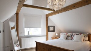 A bedroom with a wooden bed, a window with blinds, a radiator, and a hanging light fixture. - 90m² holiday house in Dhronecken (Dhronecken)