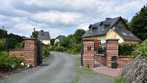 A gravel driveway leading to a gated entrance with stone pillars and a red umbrella. - 90m² holiday house in Dhronecken (Dhronecken)
