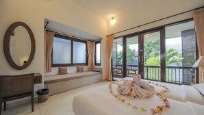 A hotel room with a large bed, a bench, a desk, and a balcony with a view of greenery. - Sayang Sanur Resort (Denpasar)