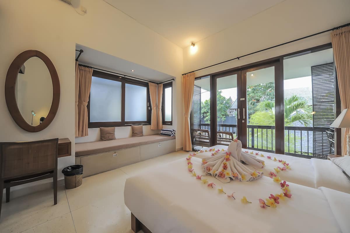 A hotel room with a large bed, a bench, a desk, and a balcony with a view of greenery.