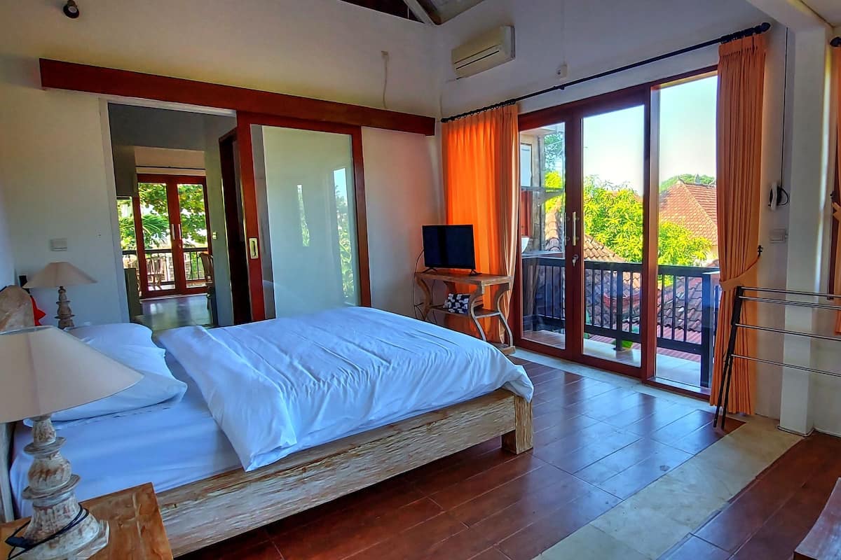 A bedroom with a bed, a desk, a chair, a TV, and a balcony with orange curtains.