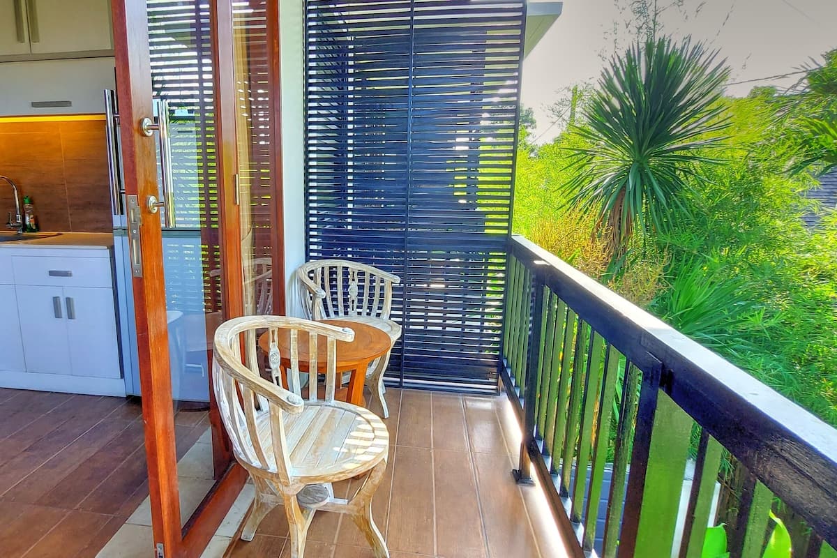 A balcony with two wicker chairs and a small table, overlooking a lush garden.
