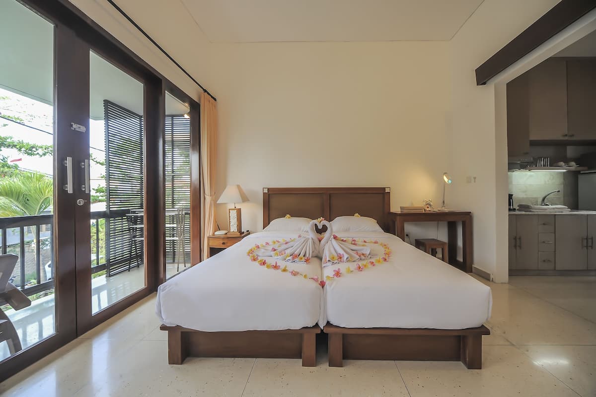 A hotel room with two beds, a balcony, a desk, and a kitchenette.