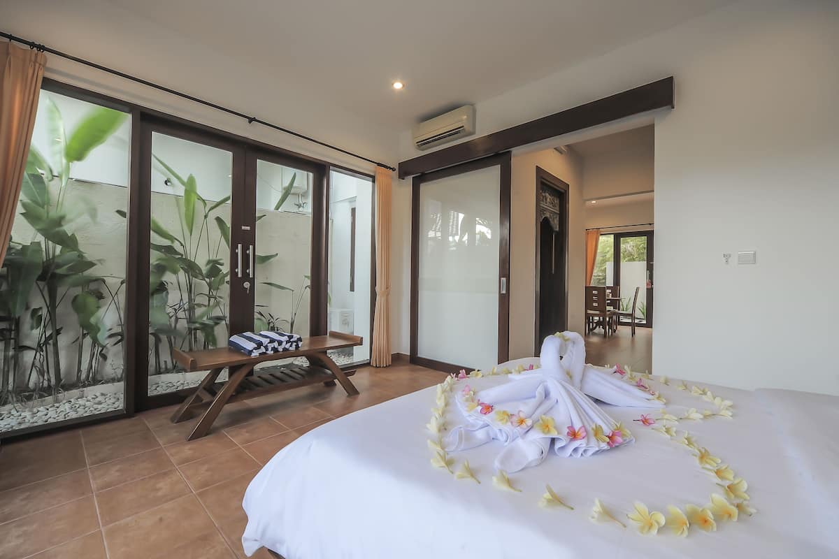 A hotel room with a bed, a bench, and a view of a garden through a sliding door.