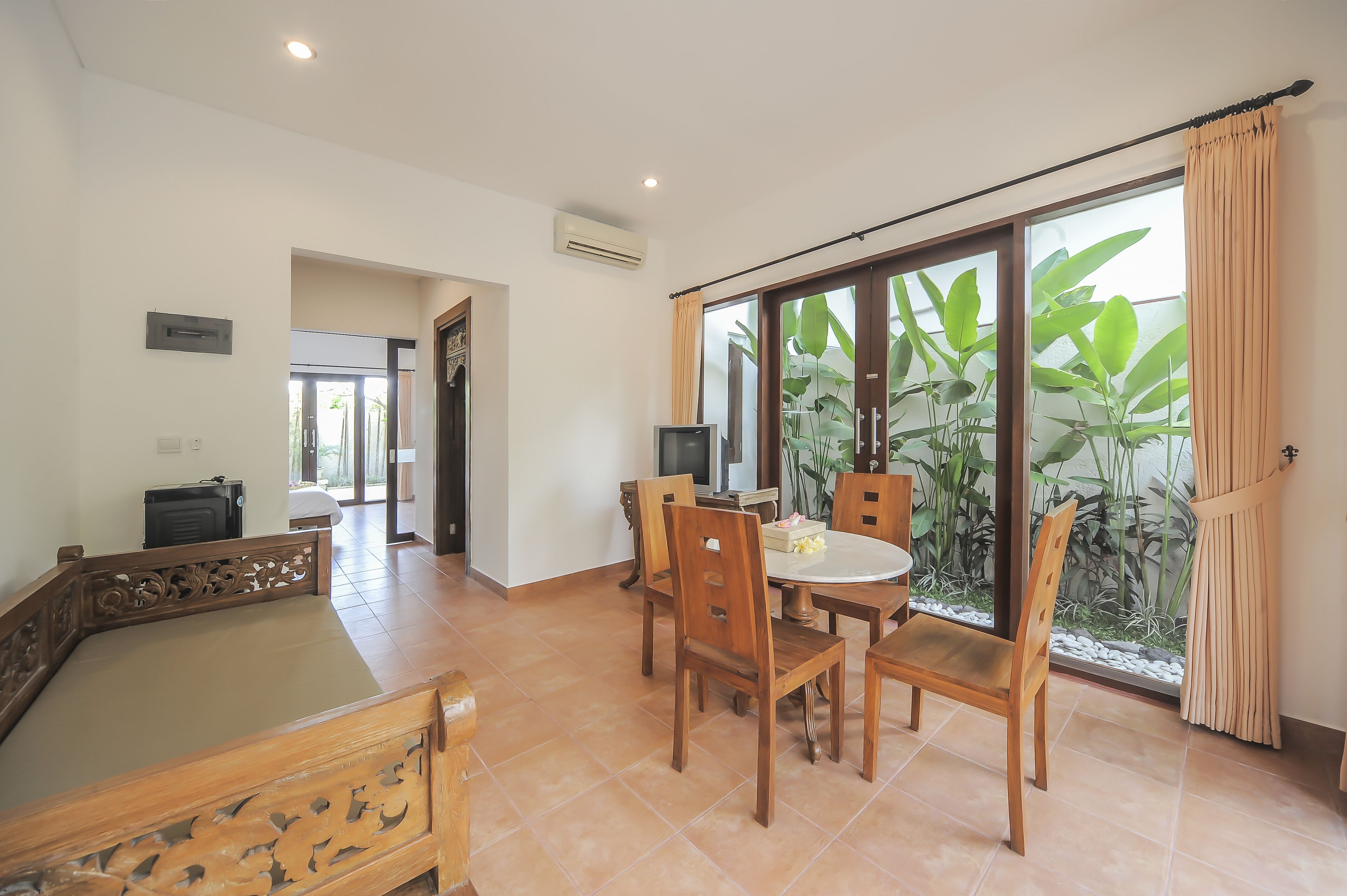 A room with a pool table, a dining area with chairs, a TV, and a large sliding glass door leading to a balcony with plants.