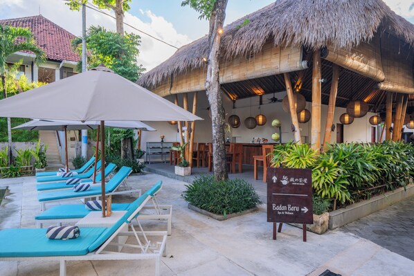 A resort with thatched-roof buildings, lounge chairs, and a sign indicating a spa and wellness center.
