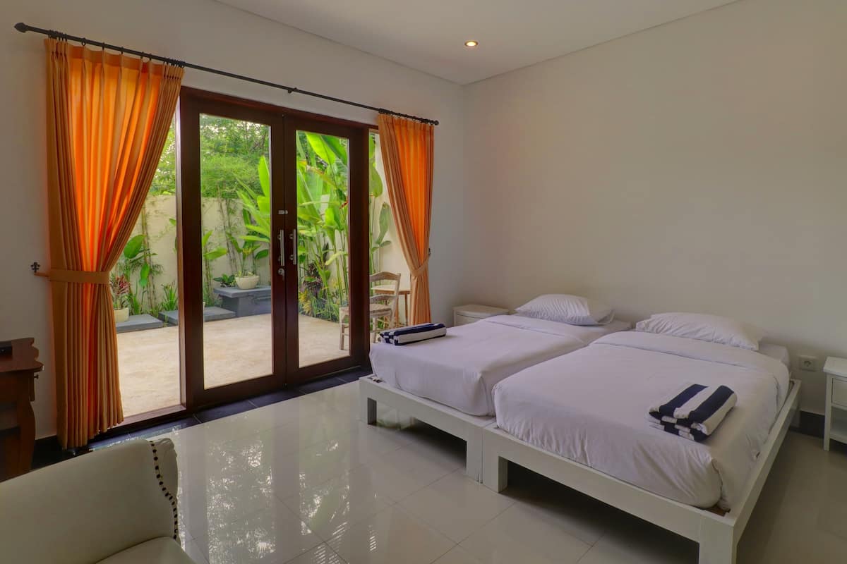 A bedroom with two beds, a sliding glass door to a garden, and a white tiled floor.