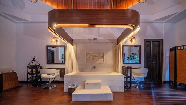 A modern bathroom with a central sink, two side mirrors, a wooden ceiling design, and a large mirror above the sink. - Sayang Sanur Resort (Denpasar)