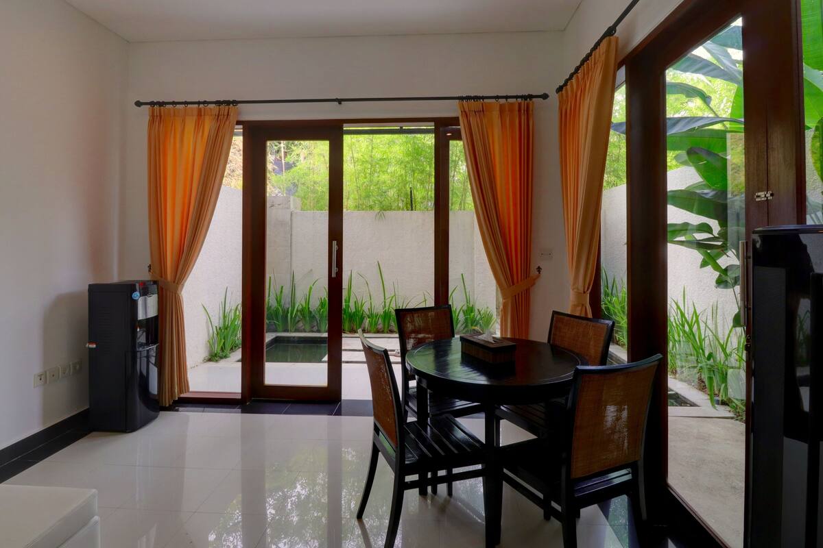 A room with a dining table and chairs, a television, and a view of greenery outside.