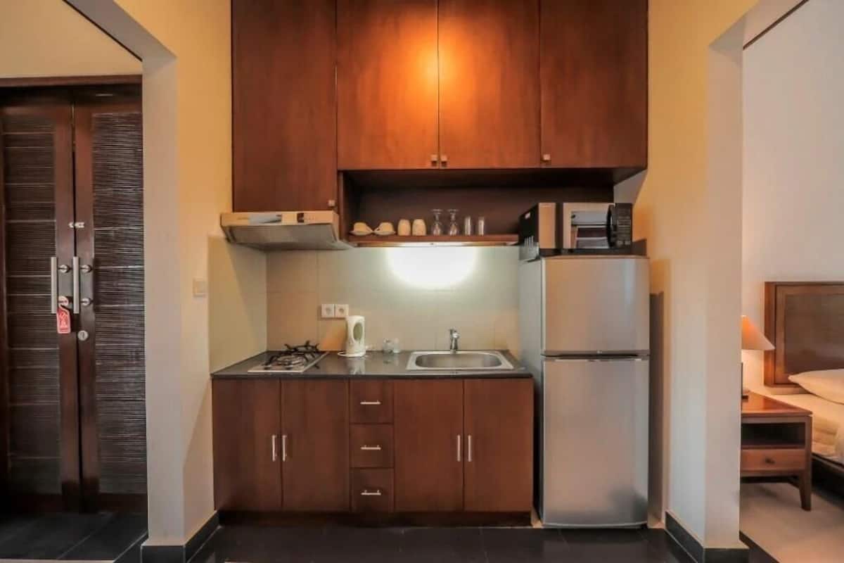 A compact kitchen with dark wooden cabinets, a stainless steel refrigerator, a built-in microwave, and a gas stove.