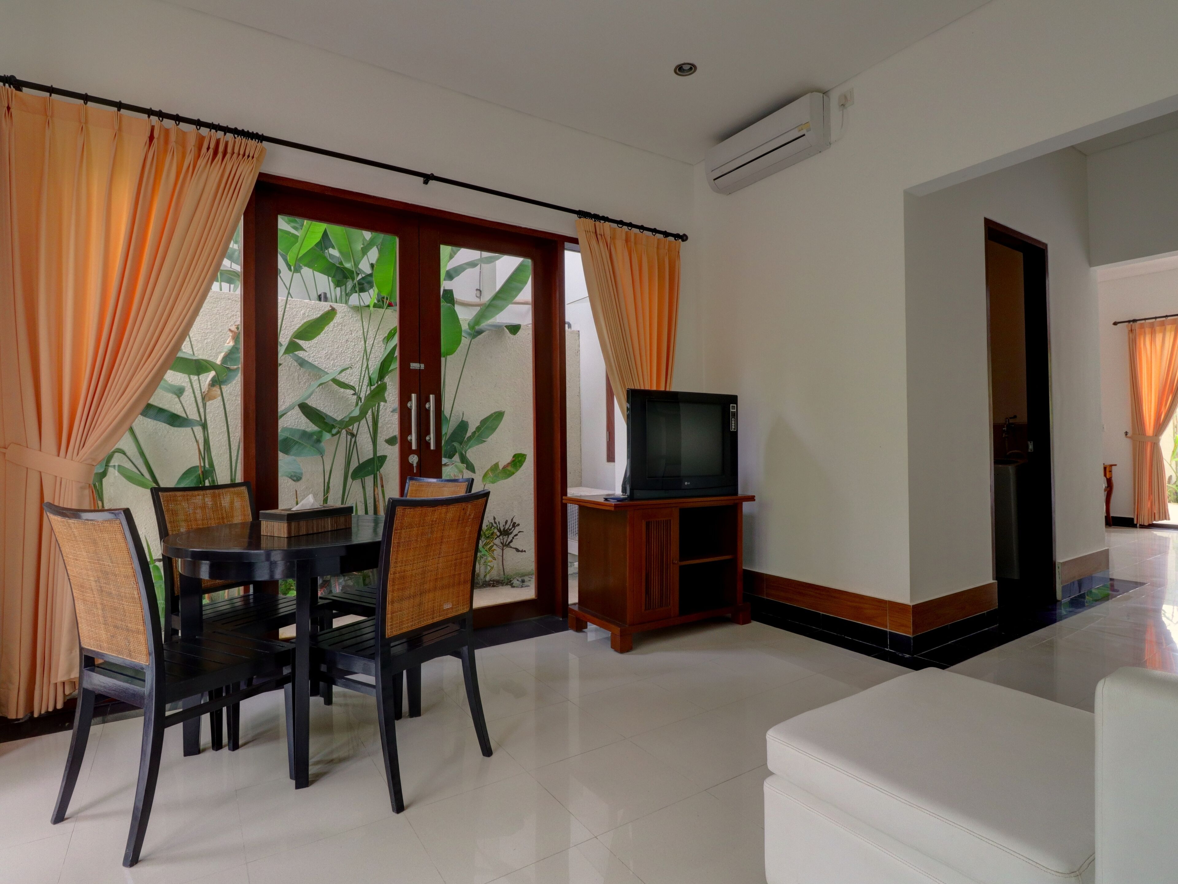 A living room with a dining area, a television on a wooden stand, and a sliding glass door with curtains.