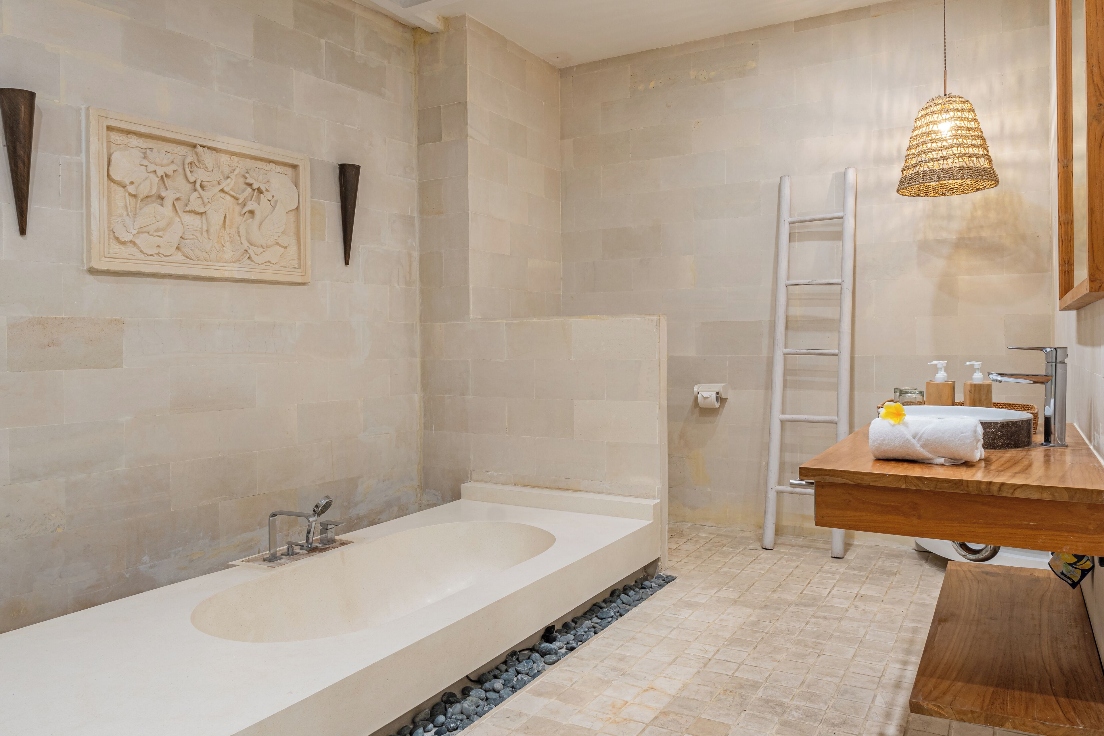 A modern bathroom with a freestanding bathtub, a wooden vanity, a towel rack, and a decorative wall piece.