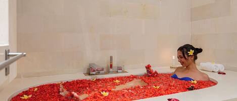 Una vasca da bagno piena di petali di rosa rossa e una donna seduta all'interno.