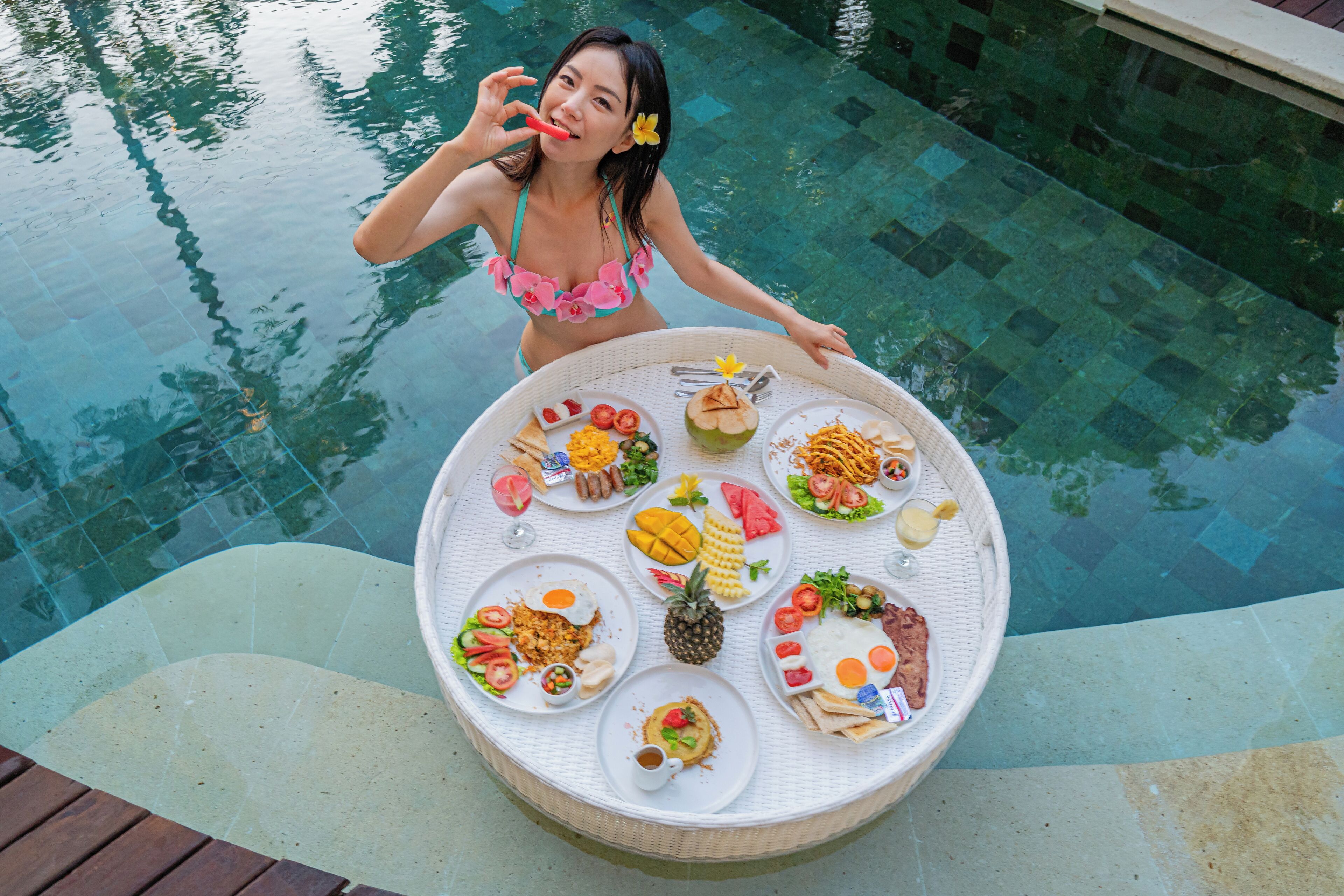 A poolside dining table with a variety of dishes, surrounded by a pool.