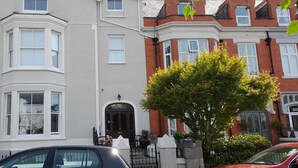 A row of terraced houses with bay windows and a tree in front. - Centrally Located Modern Apartment in Llandudno (Llandudno)