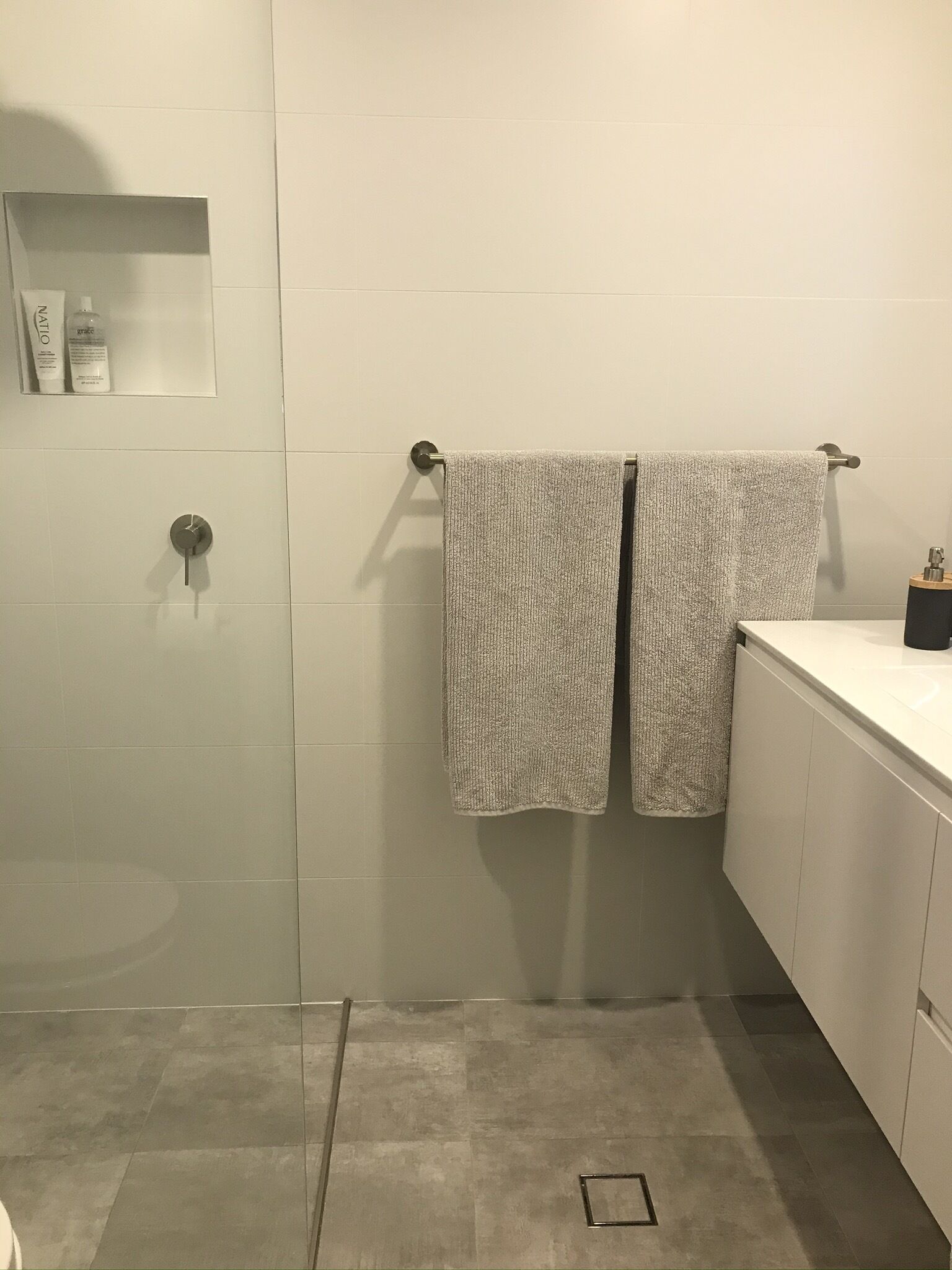 A bathroom with two towels hanging on a rack, a small shelf with toiletries, and a shower area.