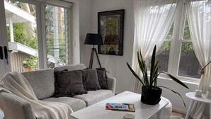 A living room with a grey sofa, a white coffee table, a potted plant, and a framed picture on the wall. - Studio minutes from Waterfront walks, close to Pasadenas, cafes, restaurants  (Bayview)