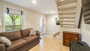 A living room with a brown sofa, a wooden cabinet, and a staircase. - Delightful Walk to Town Cottage in the Harris Lake Area | Cardinal Cottage (Highlands)