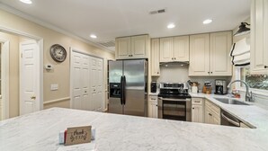 A modern kitchen with marble countertops, stainless steel appliances, and light-colored cabinetry. - Delightful Walk to Town Cottage in the Harris Lake Area | Cardinal Cottage (Highlands)