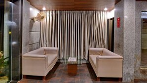A lobby with two beige sofas, a glass coffee table, and a curtain backdrop. - Gold Coast Beach Resort (Brahmagiri)