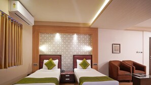 A hotel room with two beds, a brown leather armchair, a glass coffee table, and an air conditioning unit. - Gold Coast Beach Resort (Brahmagiri)