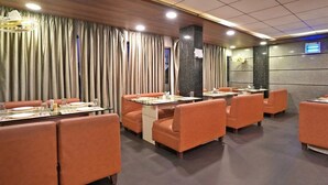A restaurant with booths and tables, wooden ceiling, and a stone wall with a digital display. - Gold Coast Beach Resort (Brahmagiri)