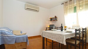 A dining area with a table set for two, a sofa with a blue cover, a wall-mounted air conditioner, and a shelf with books and a decorative item. - Apartment 2010/28524 (Istria - Stinjan), 1250m from the beach (Stinjan)