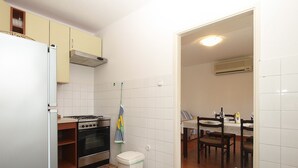 A compact kitchen with a refrigerator, stove, oven, and a small trash bin. There is a dining area with a table and chairs. - Apartment 2010/28524 (Istria - Stinjan), 1250m from the beach (Stinjan)