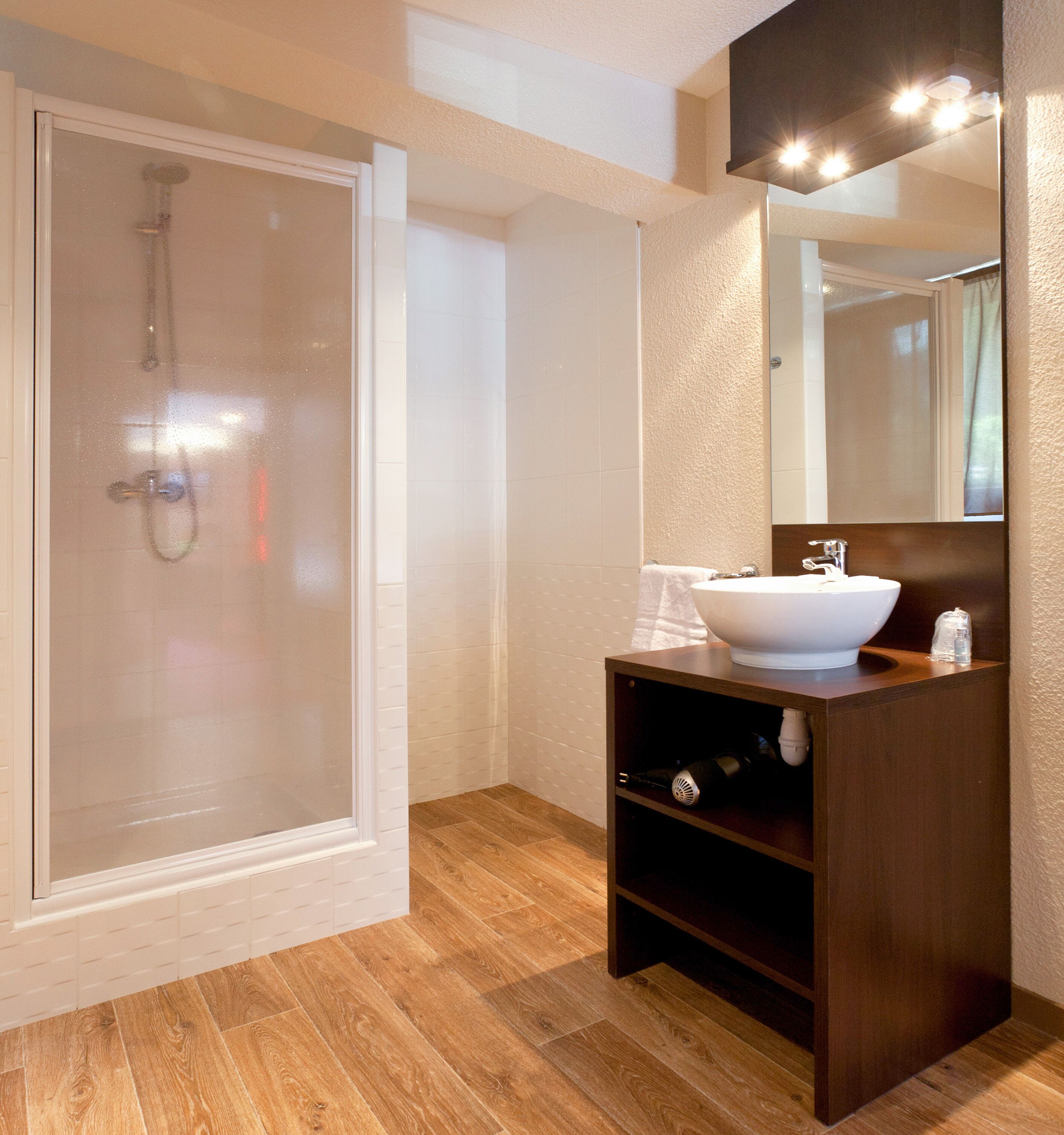A modern bathroom with a glass-enclosed shower, a wooden vanity with a white sink, and a large mirror.
