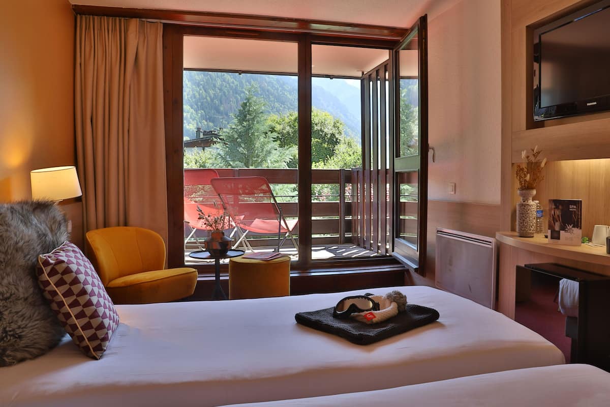 Ein Hotelzimmer mit einem großen Bett, einer Couch, einem Fernseher, einem Balkon mit Bergblick und einem Tisch mit einem Tablett Essen.