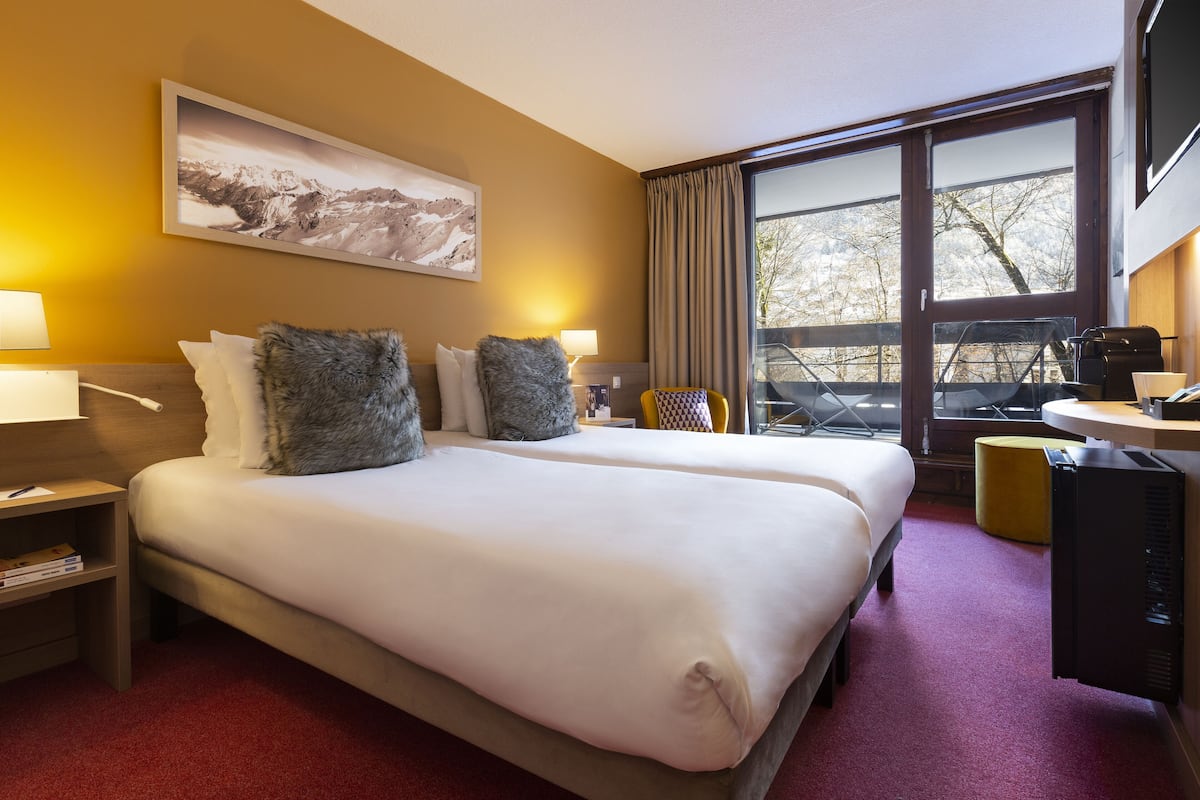 Ein Hotelzimmer mit zwei Betten, einem großen Fenster, einem Schreibtisch und einem Stuhl.