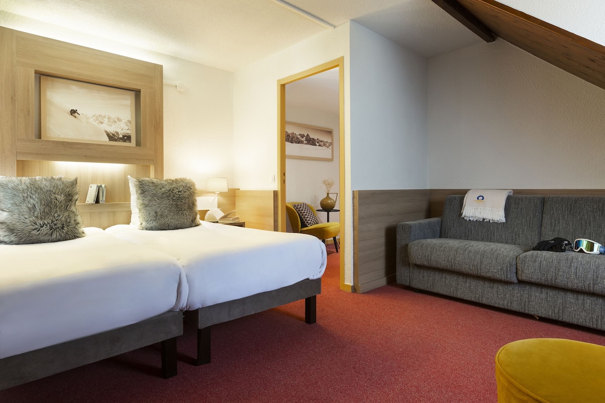 Ein Hotelzimmer mit einem Bett, einer Couch, einem gelben Sessel und einem an einer Holzleiste befestigten Bild.