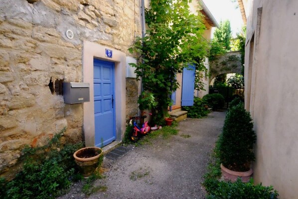 A narrow alley with stone buildings, a blue door, and a small garden area with a bicycle and potted plants. - House with terrace in the heart of Provence (Bonnieux)