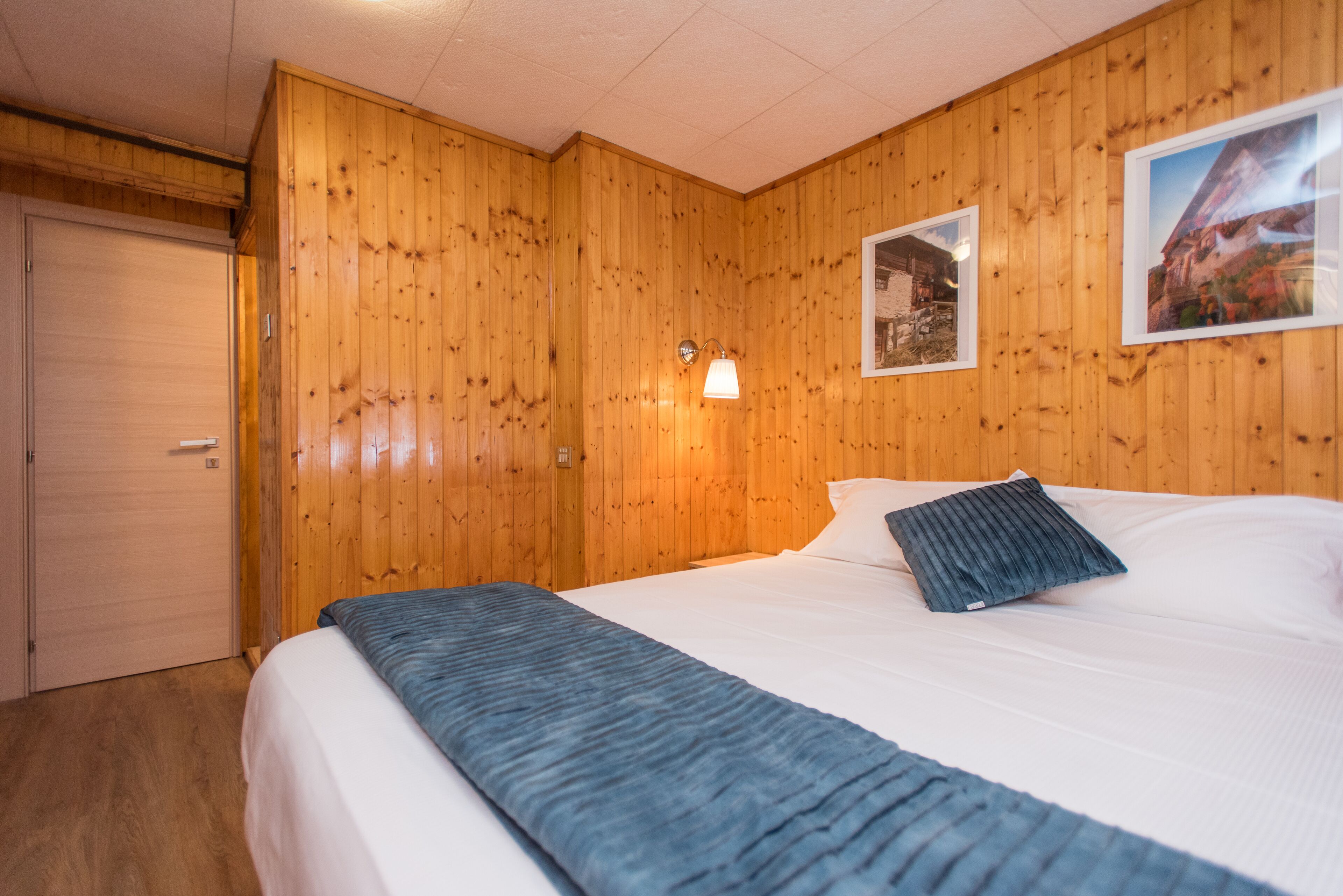Una habitación con paneles de madera, una cama, una mesita de noche, una lámpara de pared y una puerta.