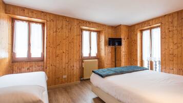 A room with wooden walls, two beds, a TV mounted on the wall, and a window.