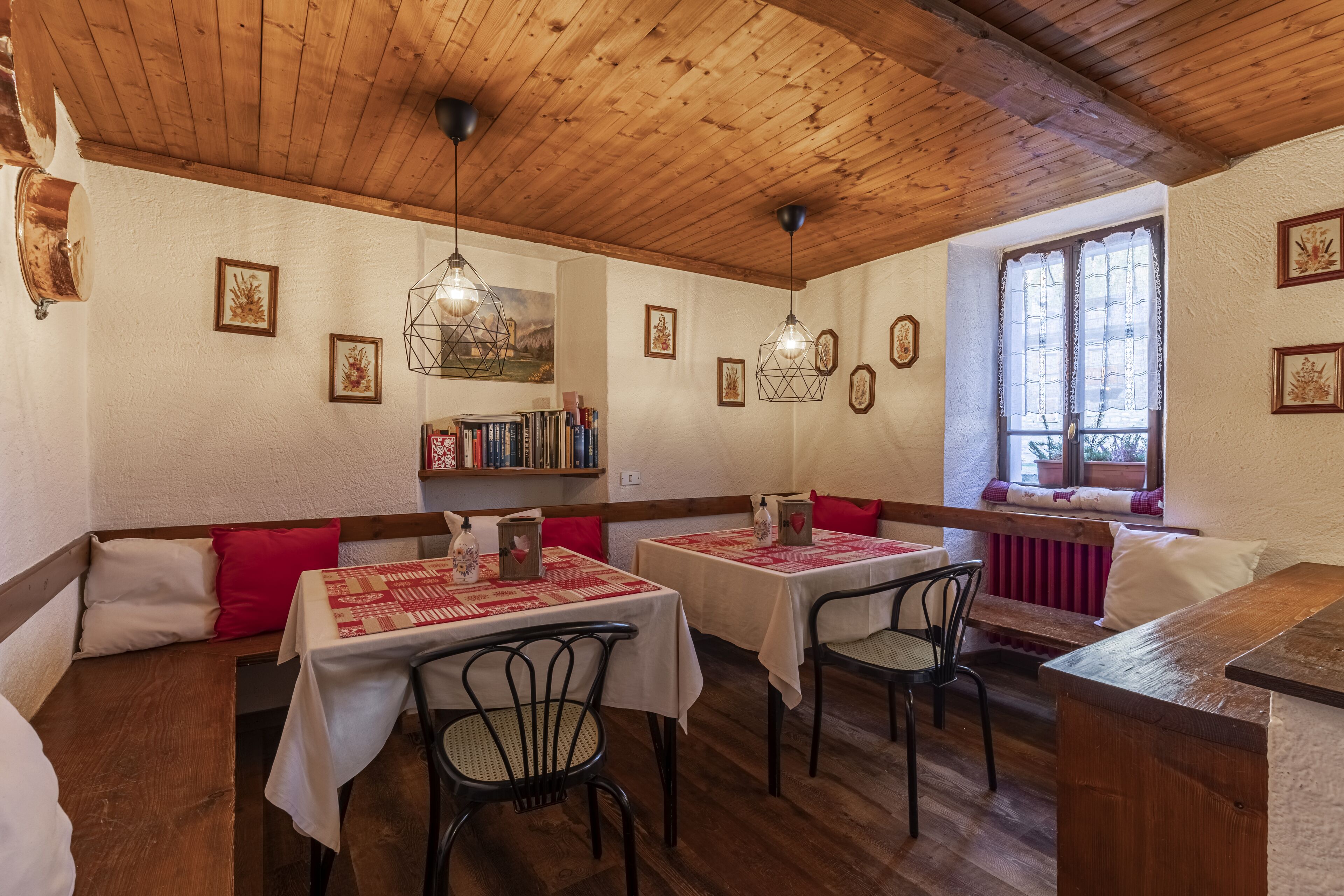 A cozy dining area with wooden tables and benches, surrounded by bookshelves and framed pictures.