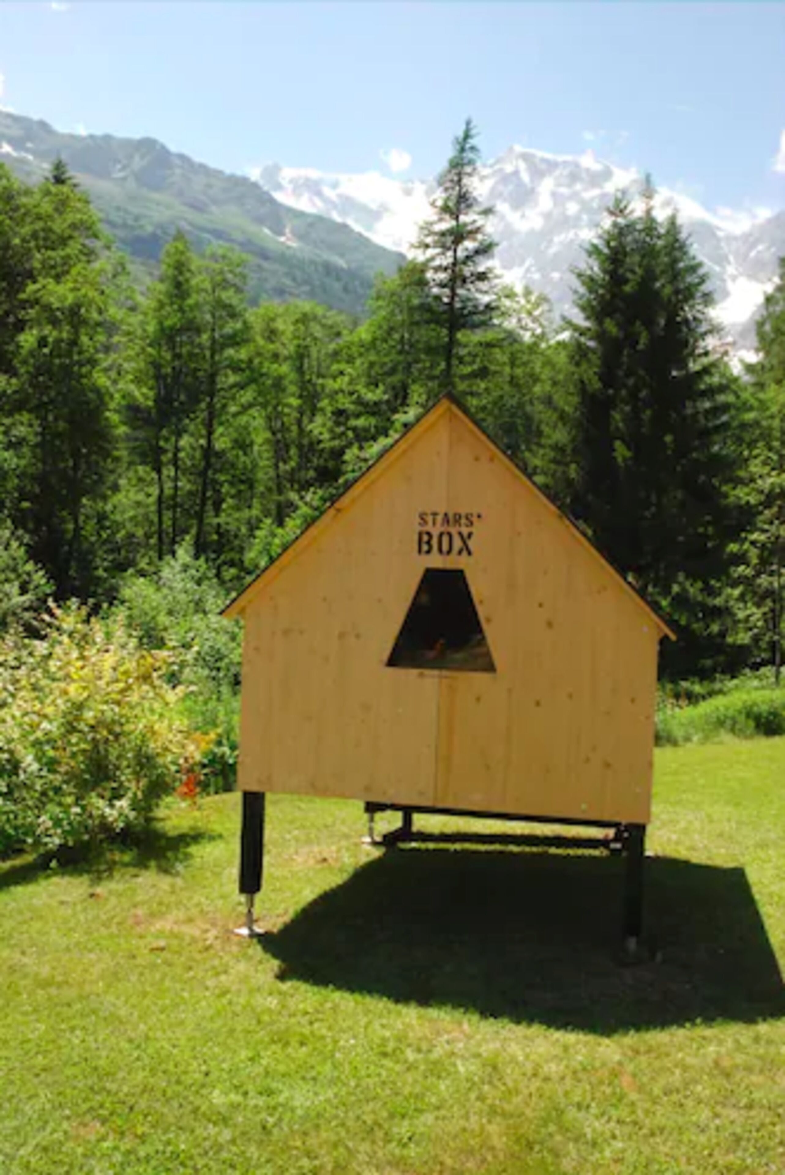 Une structure en bois portant l’inscription « Boîte des étoiles », située dans un champ herbeux avec une chaîne de montagnes en arrière-plan.