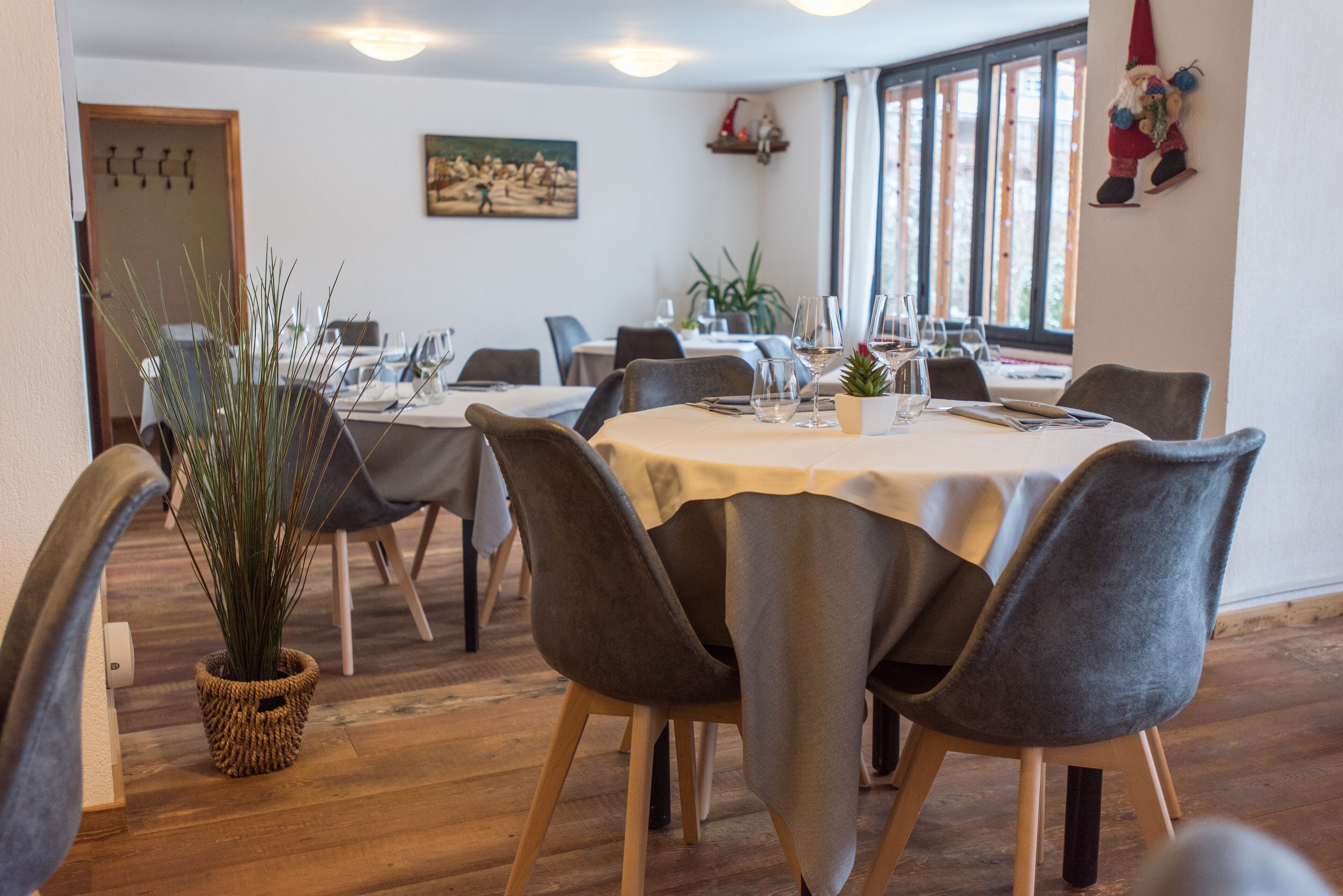 Een eetgedeelte met ronde tafels, grijze gestoffeerde stoelen en een potplant.